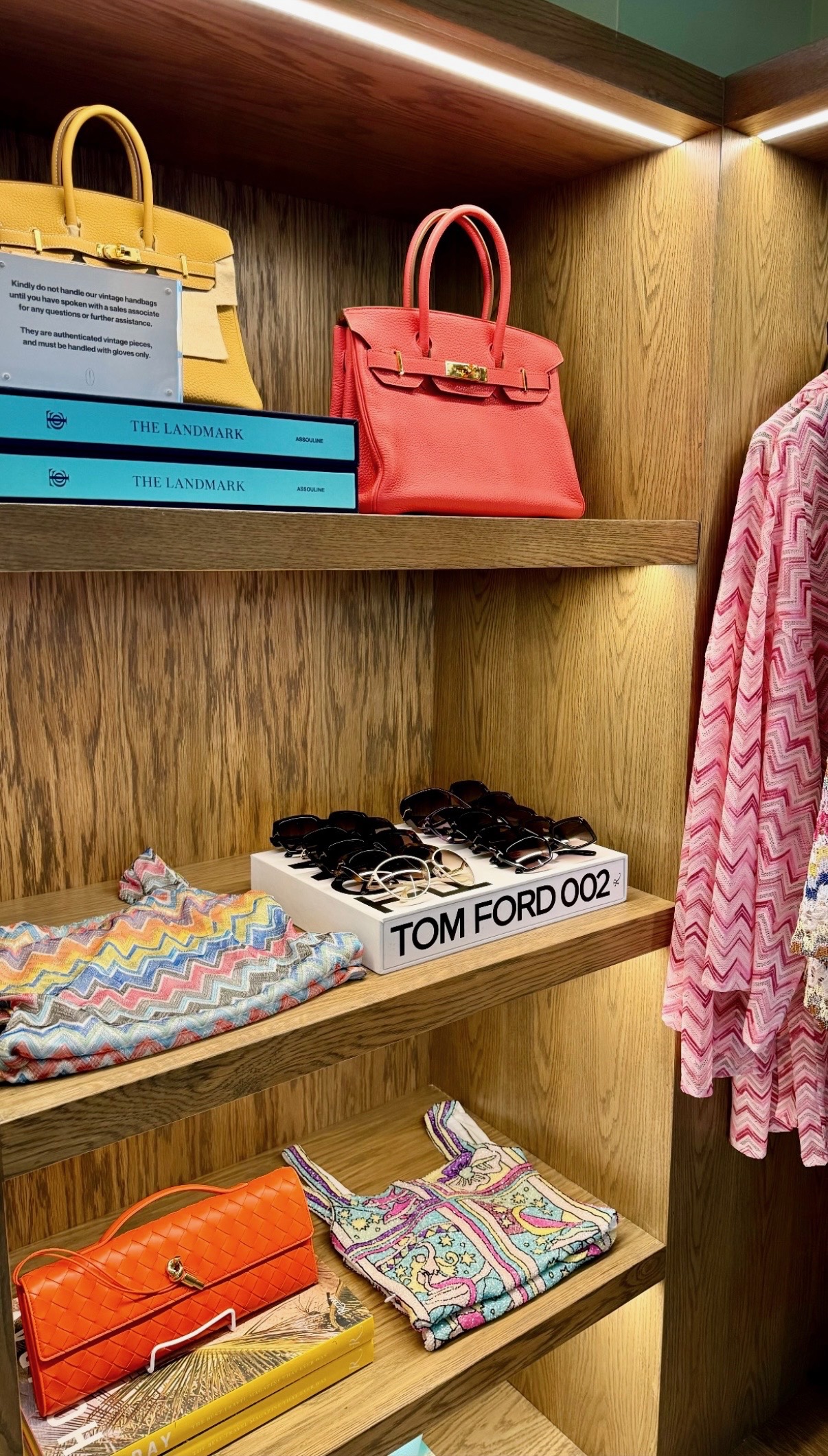 Luxury handbags, sunglasses, books, and patterned resort apparel displayed on warm wood shelves in Anguilla
