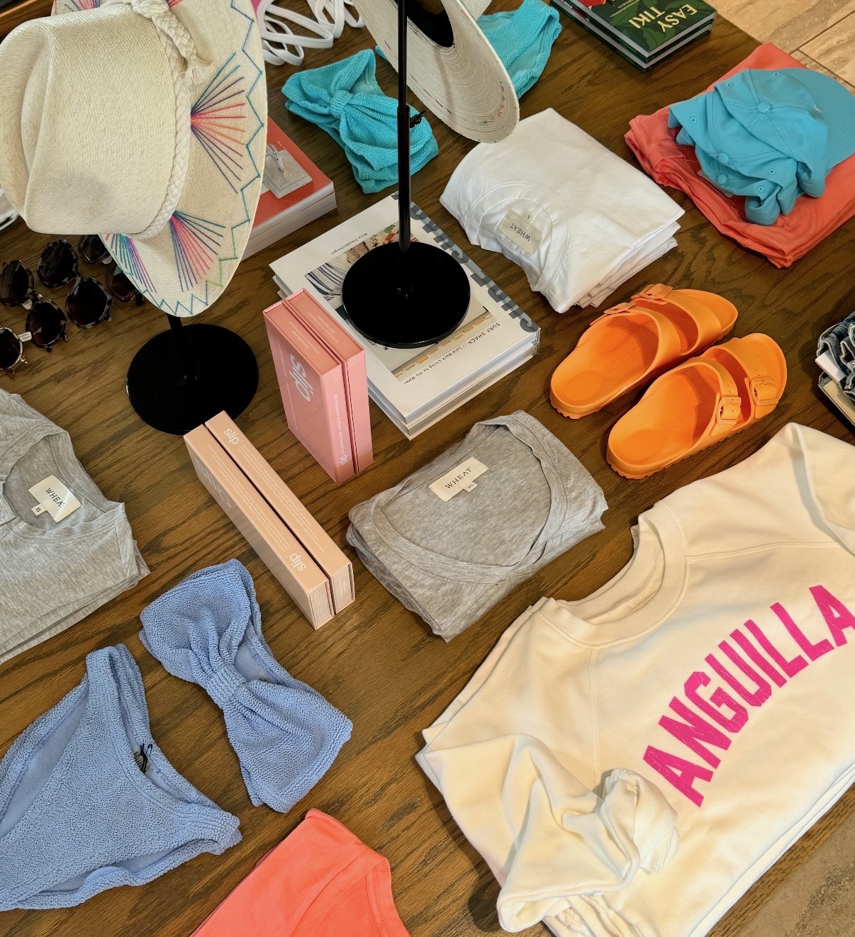 Hats, apparel, bright sandals, books, and accessories styled on a wood table in Anguilla