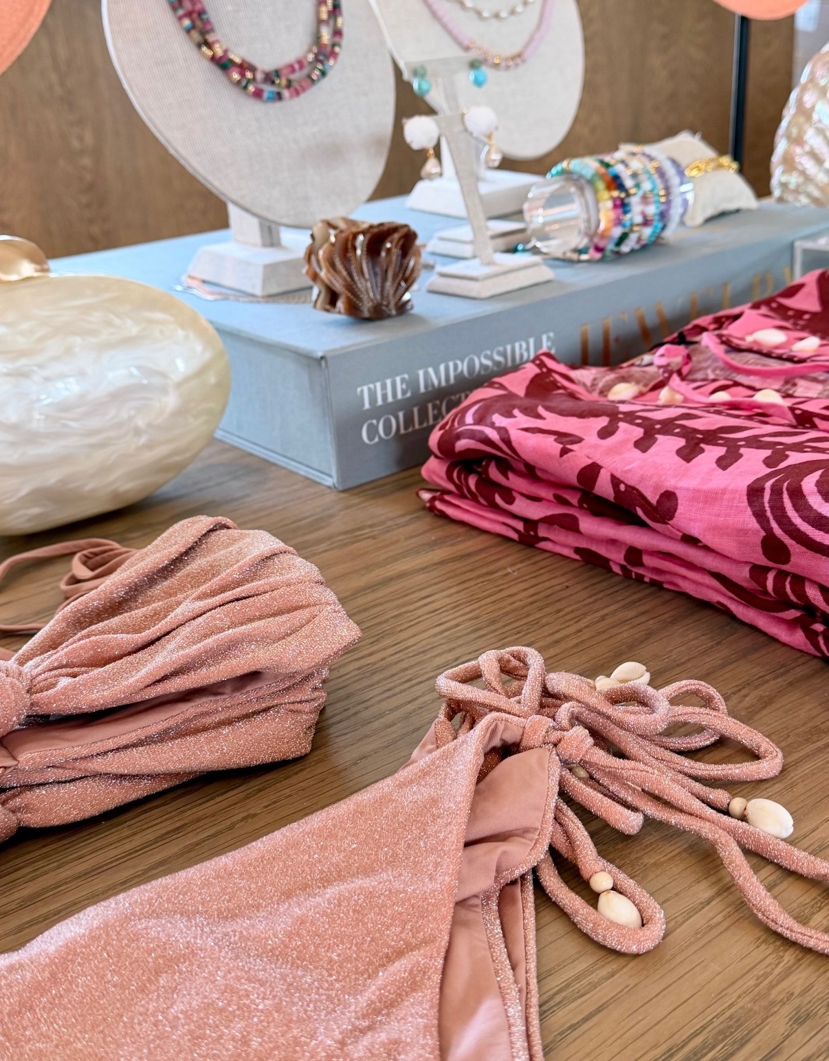 Blush swimwear, colorful jewelry, folded apparel, and accessories arranged on a wood table in Anguilla