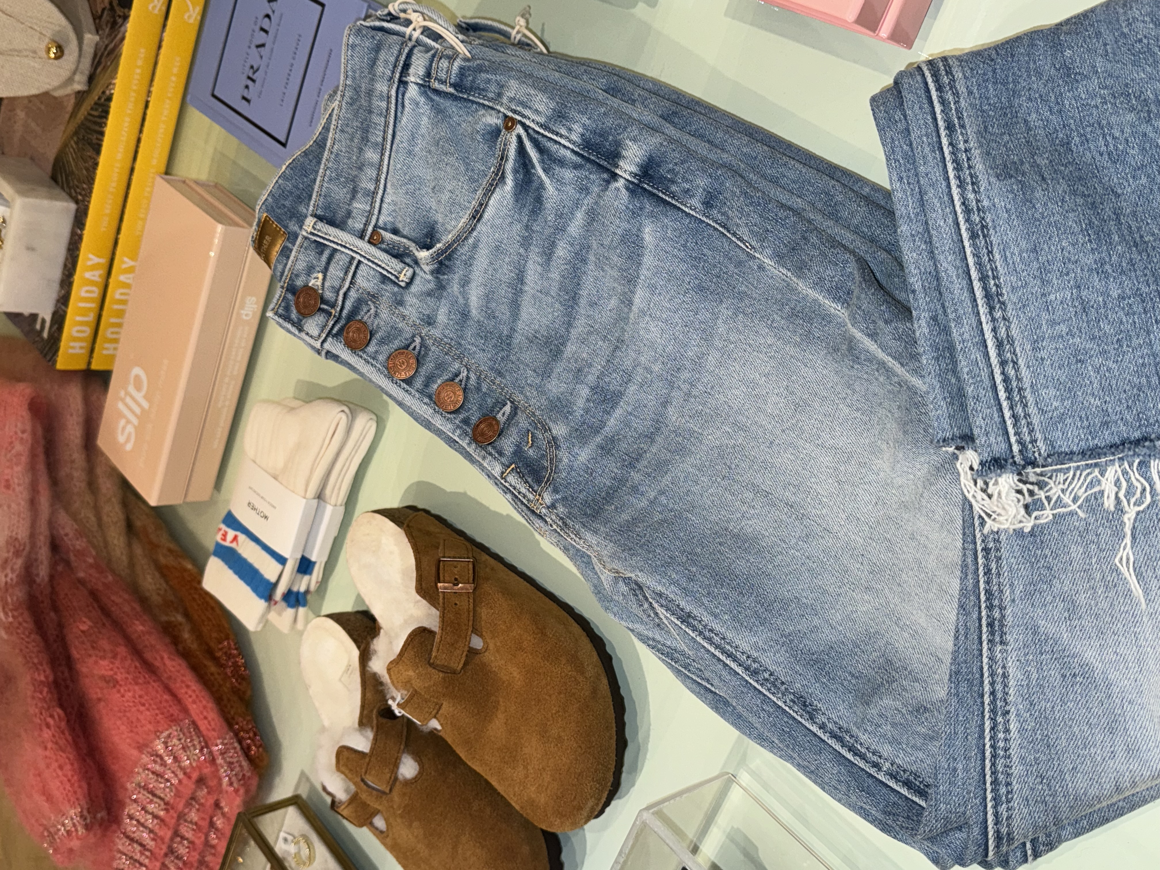 Denim, footwear, knitwear, jewelry, and books styled into a coordinated boutique tabletop story