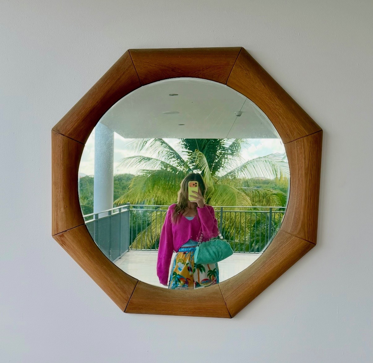 Emily Maroney reflected in a sculptural wood-framed mirror with palms beyond the balcony