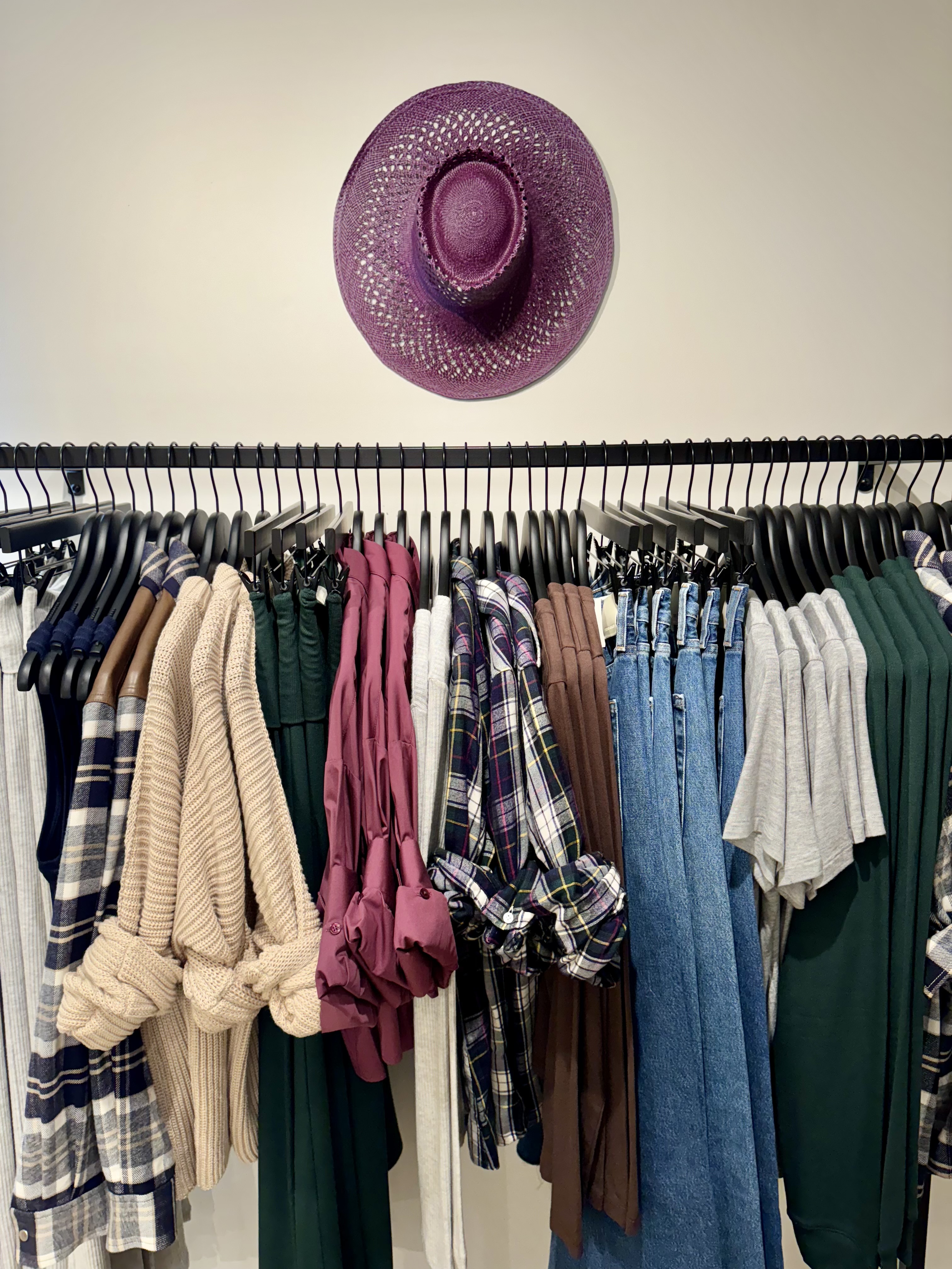 Apparel rail organized by color, texture, and silhouette beneath a sculptural purple hat