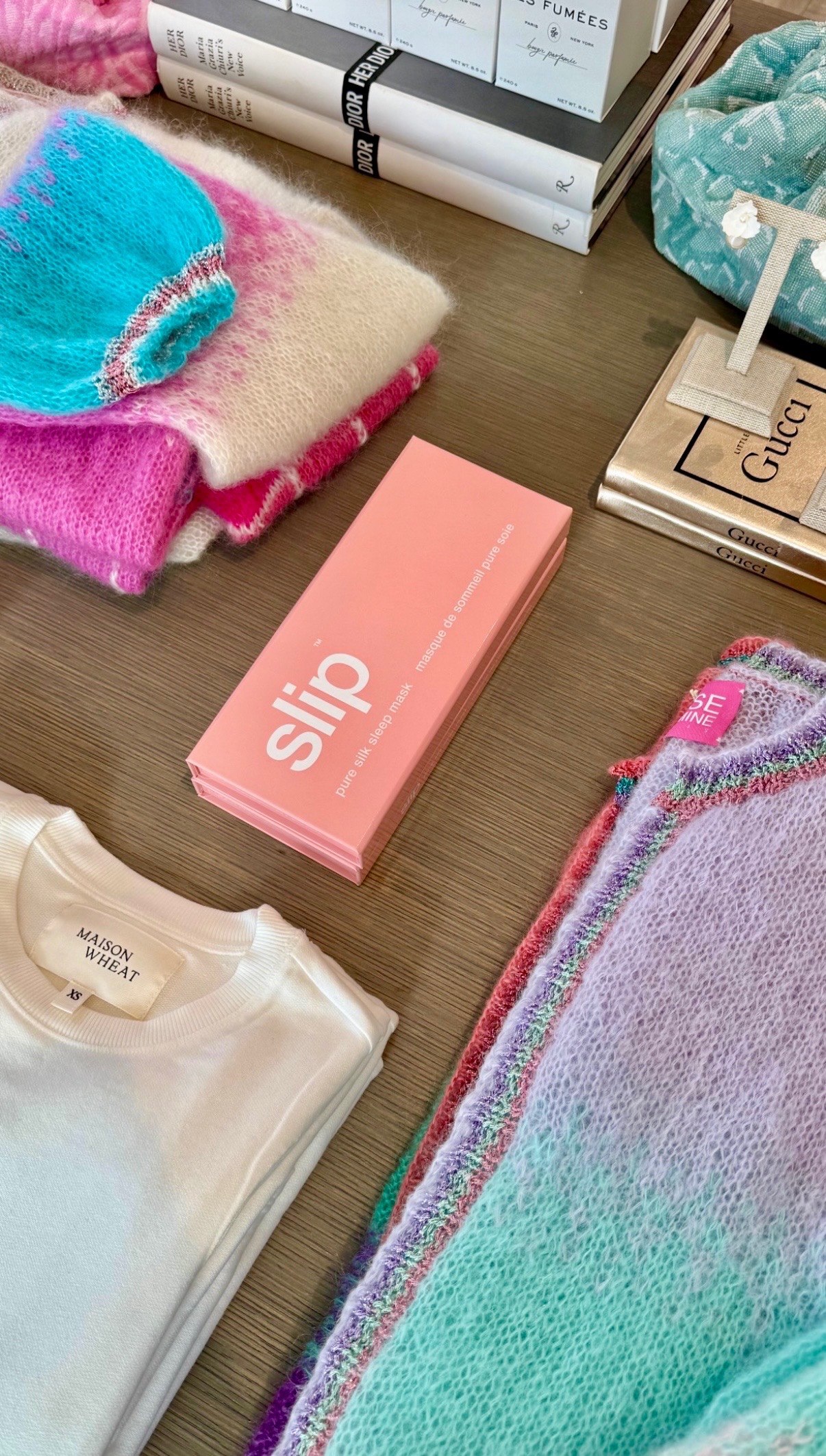 Colorful knitwear, fashion books, beauty products, and folded apparel styled on a Nantucket table