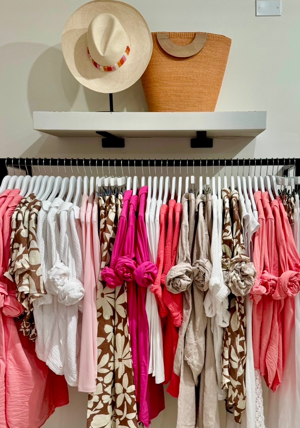 Pink, coral, neutral, and floral resort apparel arranged beneath a straw hat and woven tote