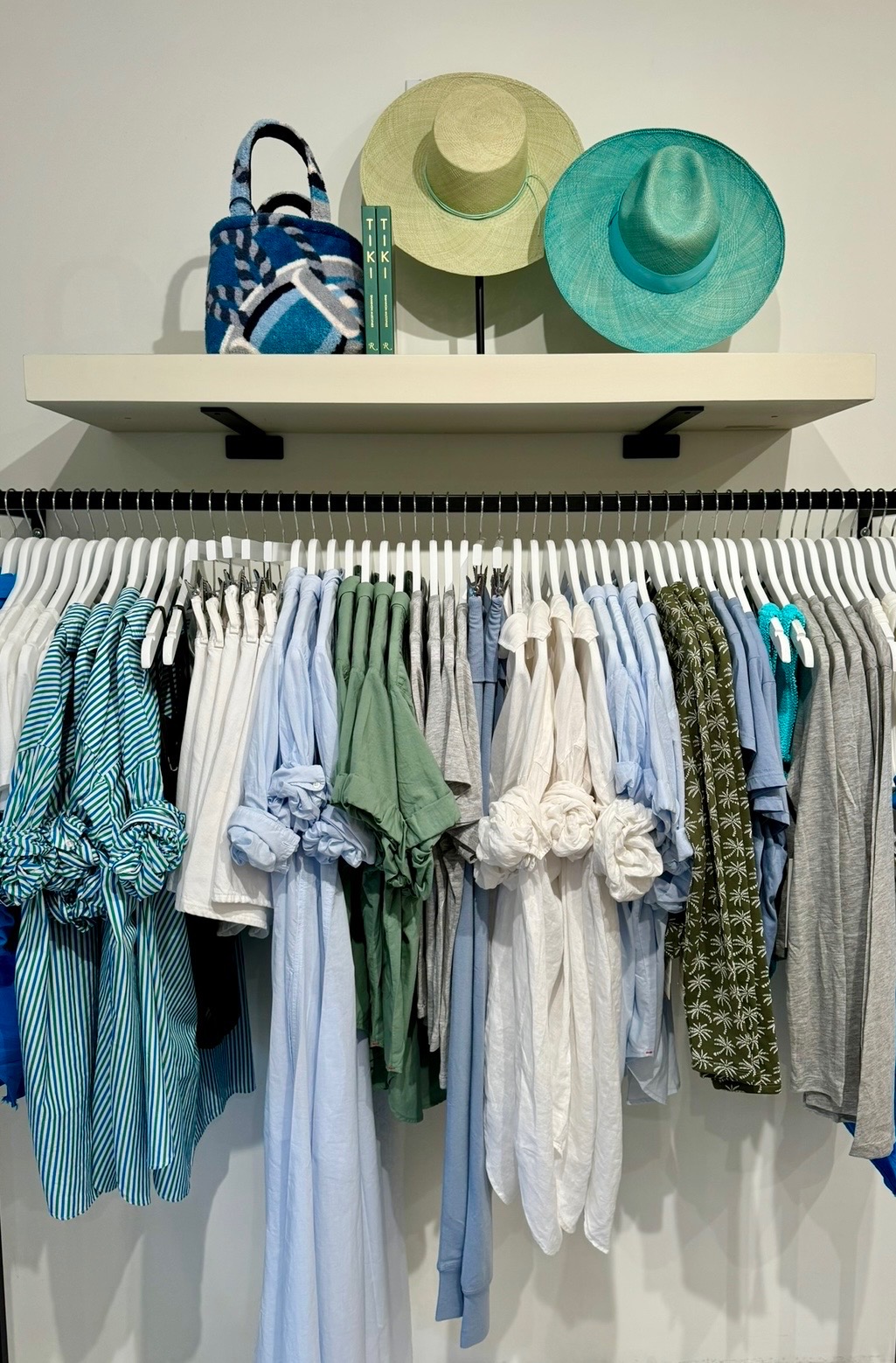 Blue, green, white, and striped resort apparel displayed beneath woven hats and accessories
